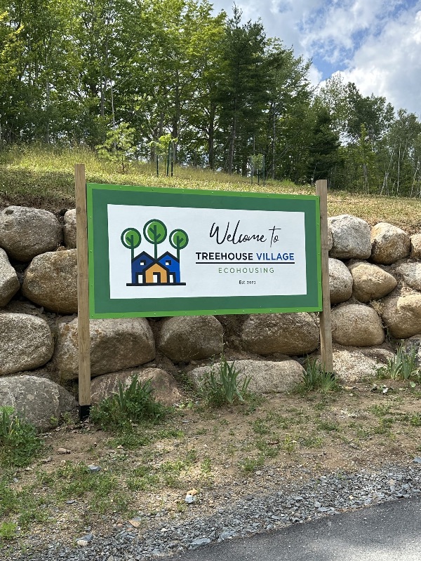 Sign for Treehouse Village Ecohousing with trees and rocks in background.