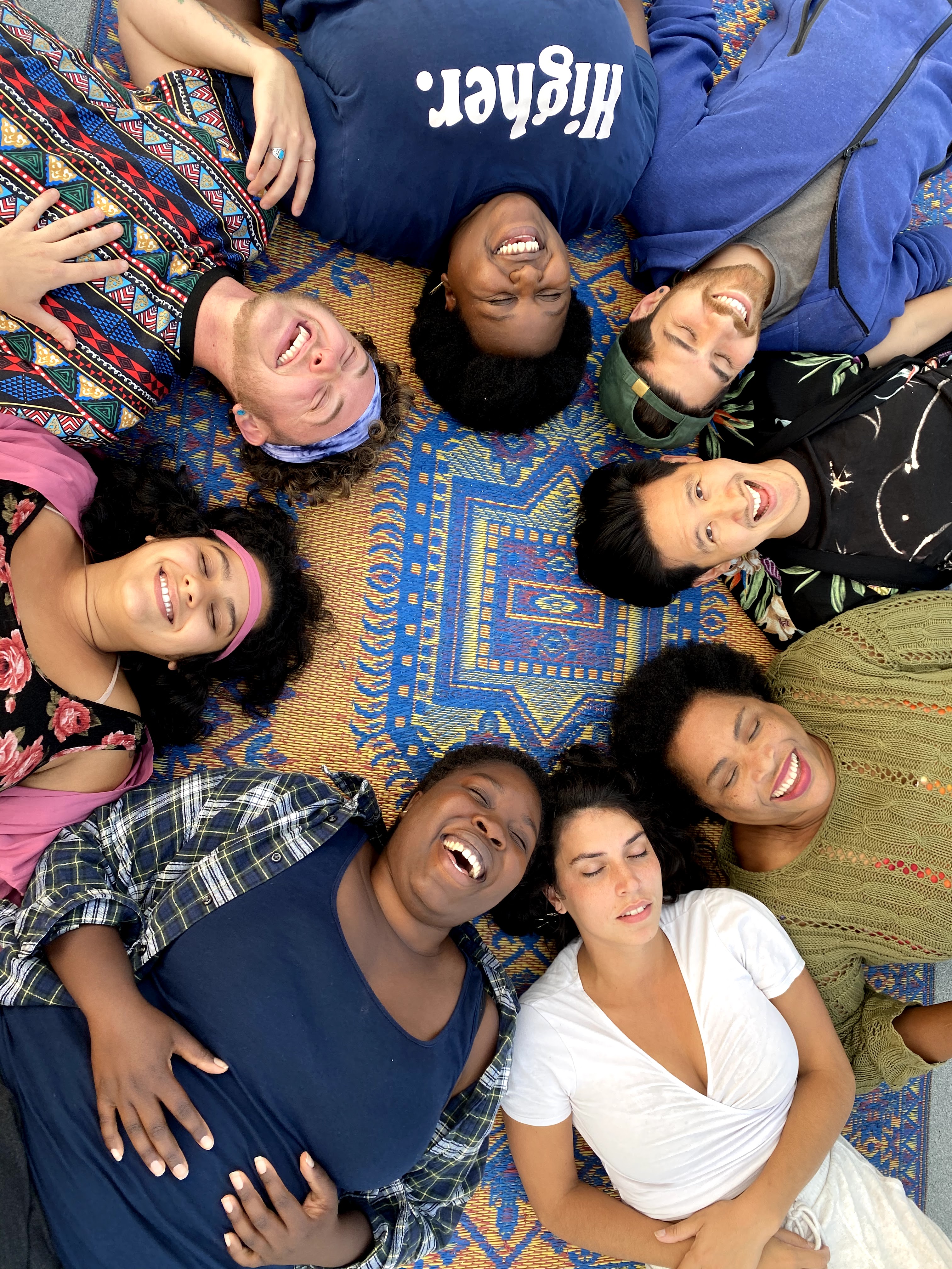 Group of smiling diverse people lying on a vibrant patterned rug.