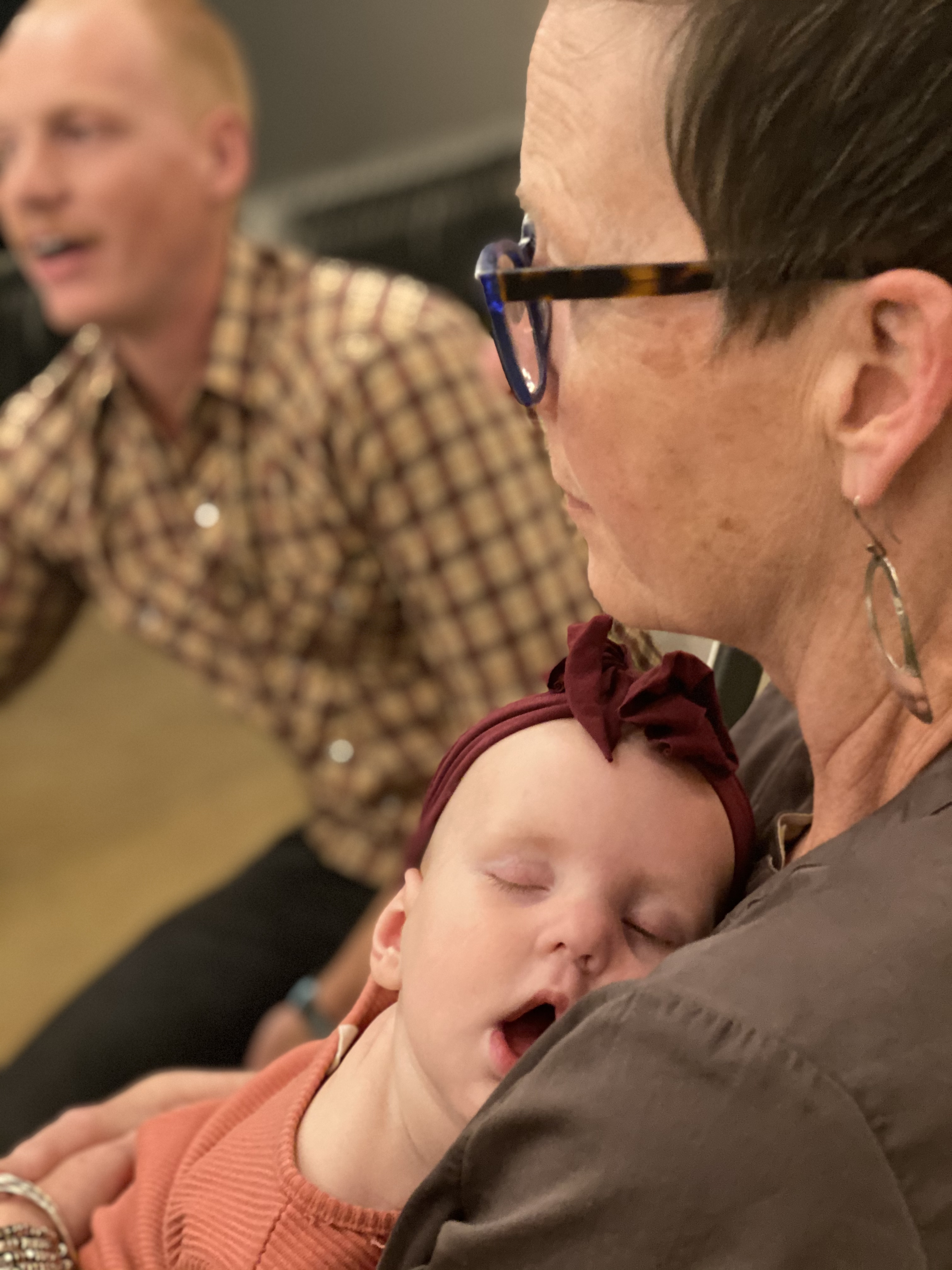 Woman holding sleeping child with man in background at community event.