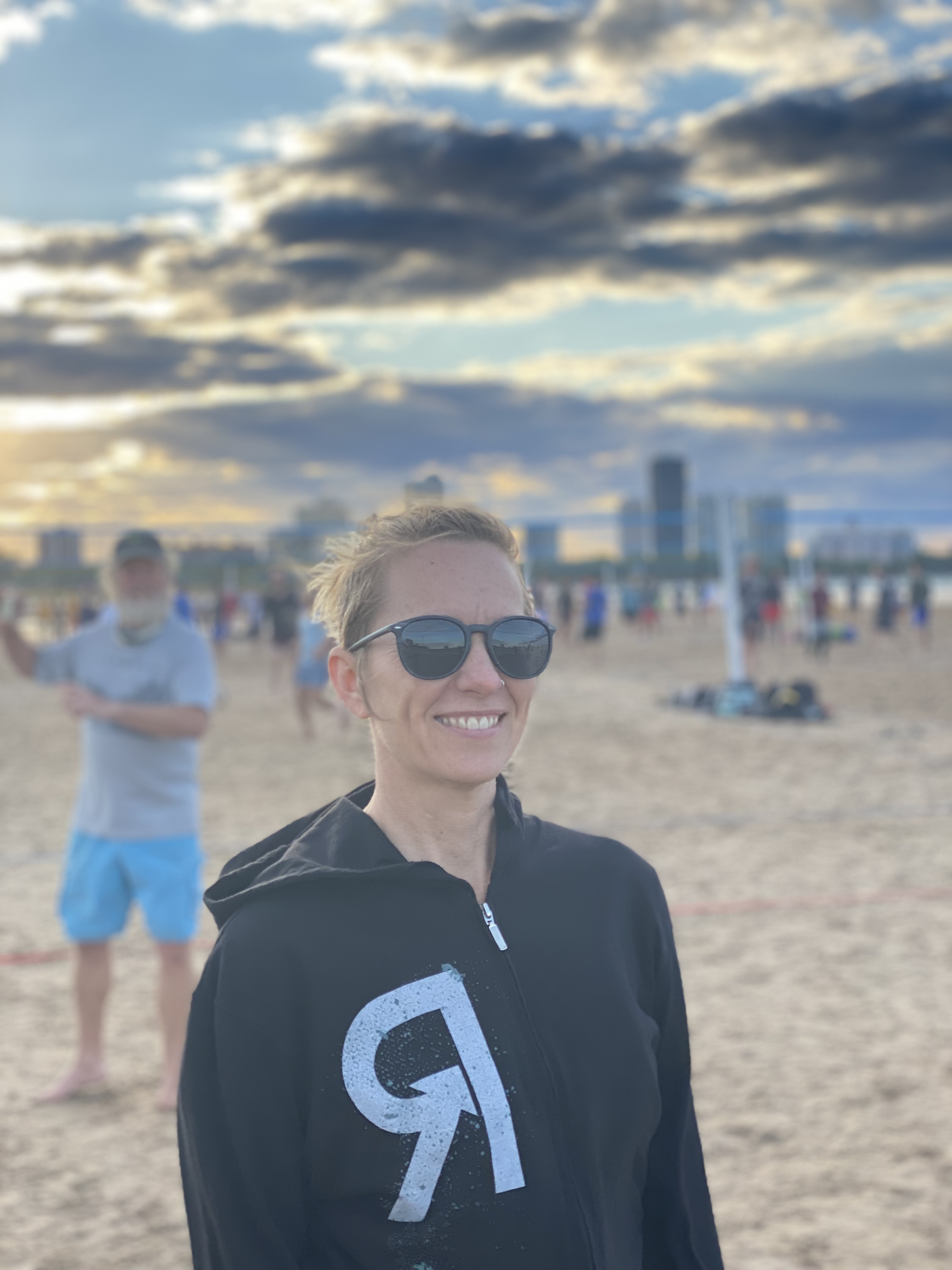 Woman with sunglasses smiling at beach during sunset.