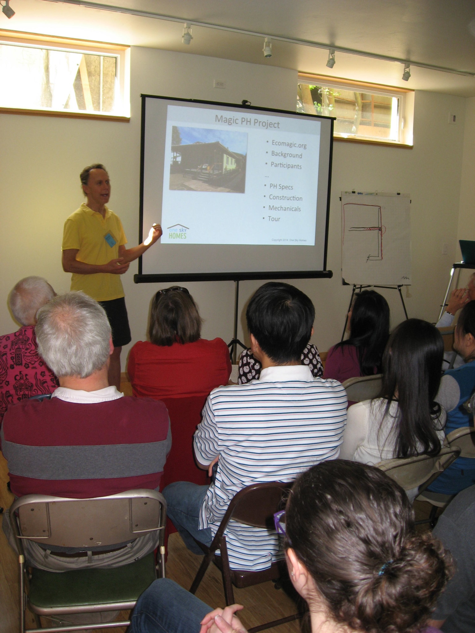 Speaker presenting on intentional community projects to engaged audience.