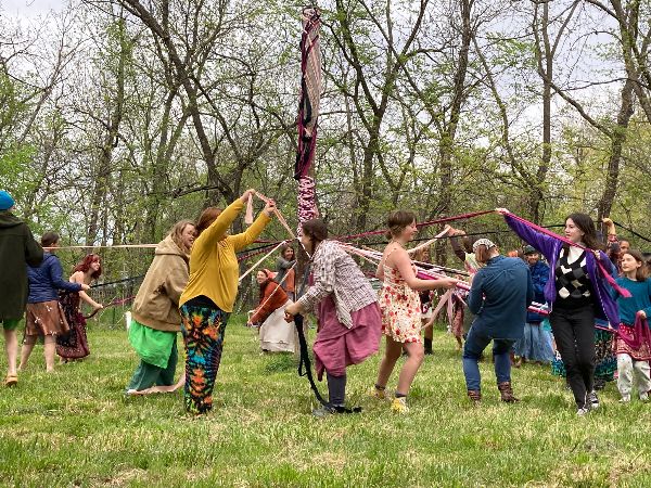 People dancing and playing with ribbons in a green outdoor setting.