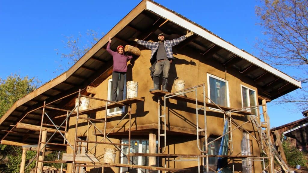 Two people standing on scaffolding in front of a sustainable eco-home.