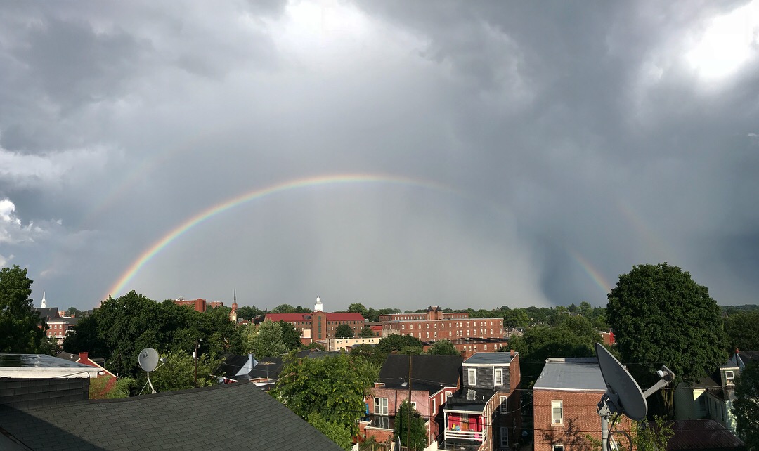 Double rainbow over urban neighborhood with dark storm clouds.