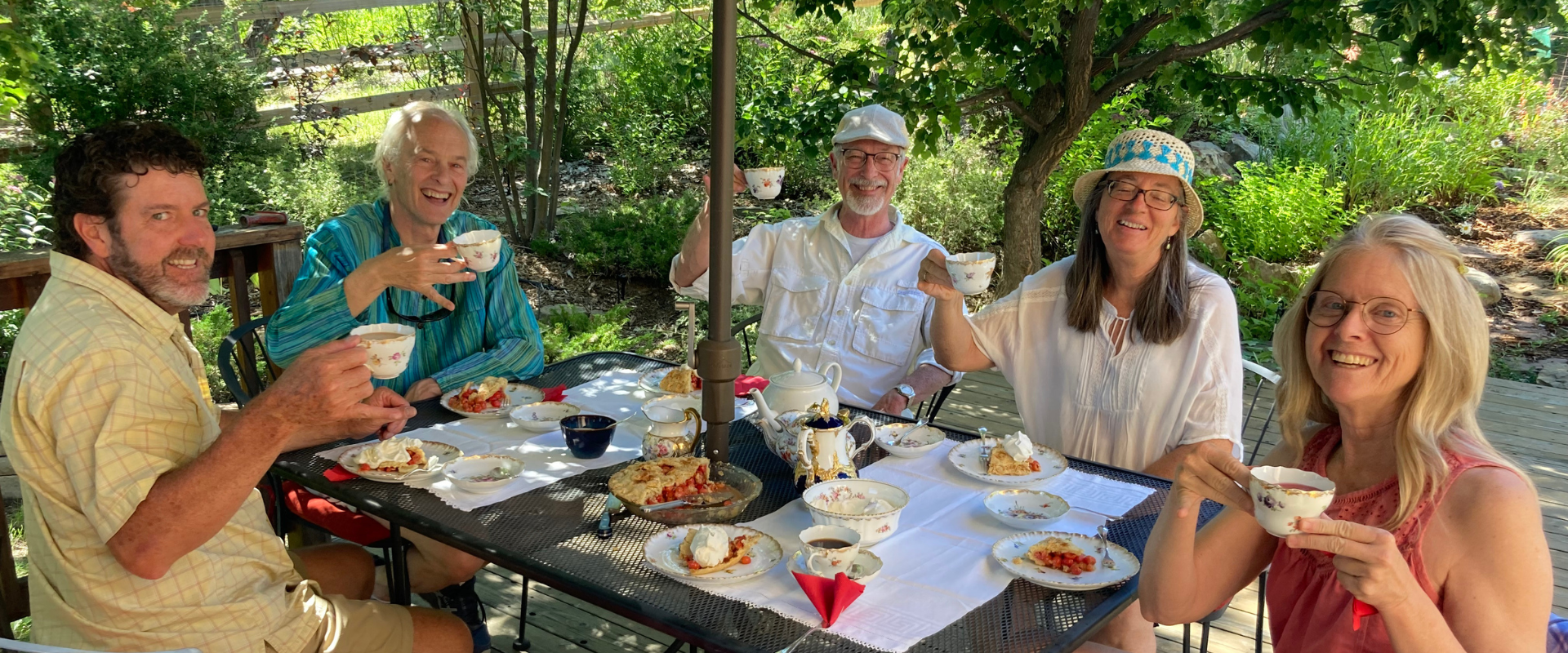 Group of people enjoying a meal outdoors in a lush garden setting.