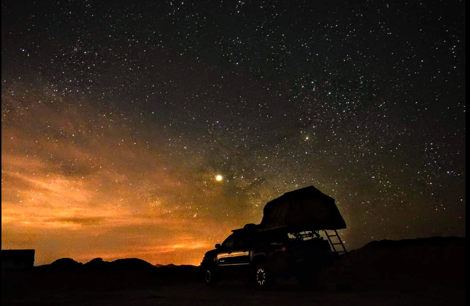 Night sky filled with stars over a vehicle with a rooftop tent.