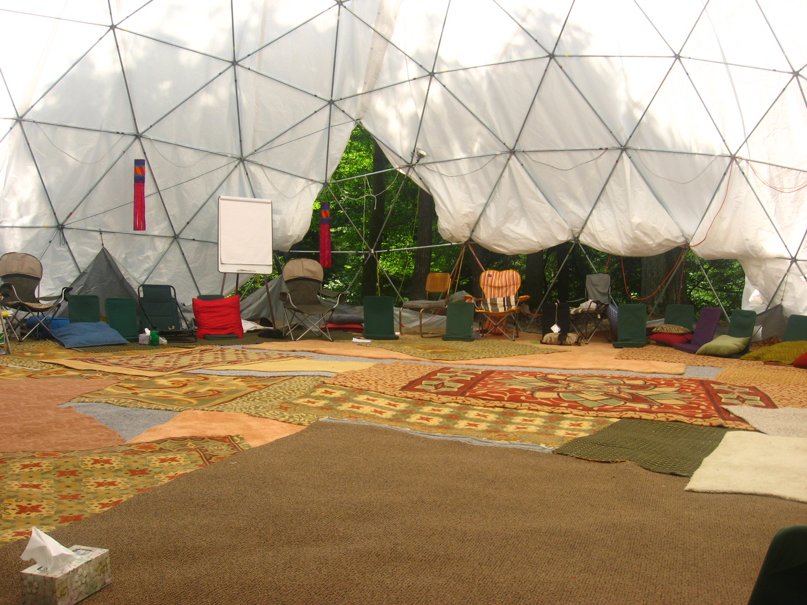 Interior of geodesic dome with seating and colorful rugs for community gatherings.