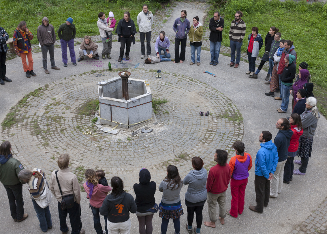 Group of people gathered around a fire pit in a circle at Hofkollektiv Zwetschke.