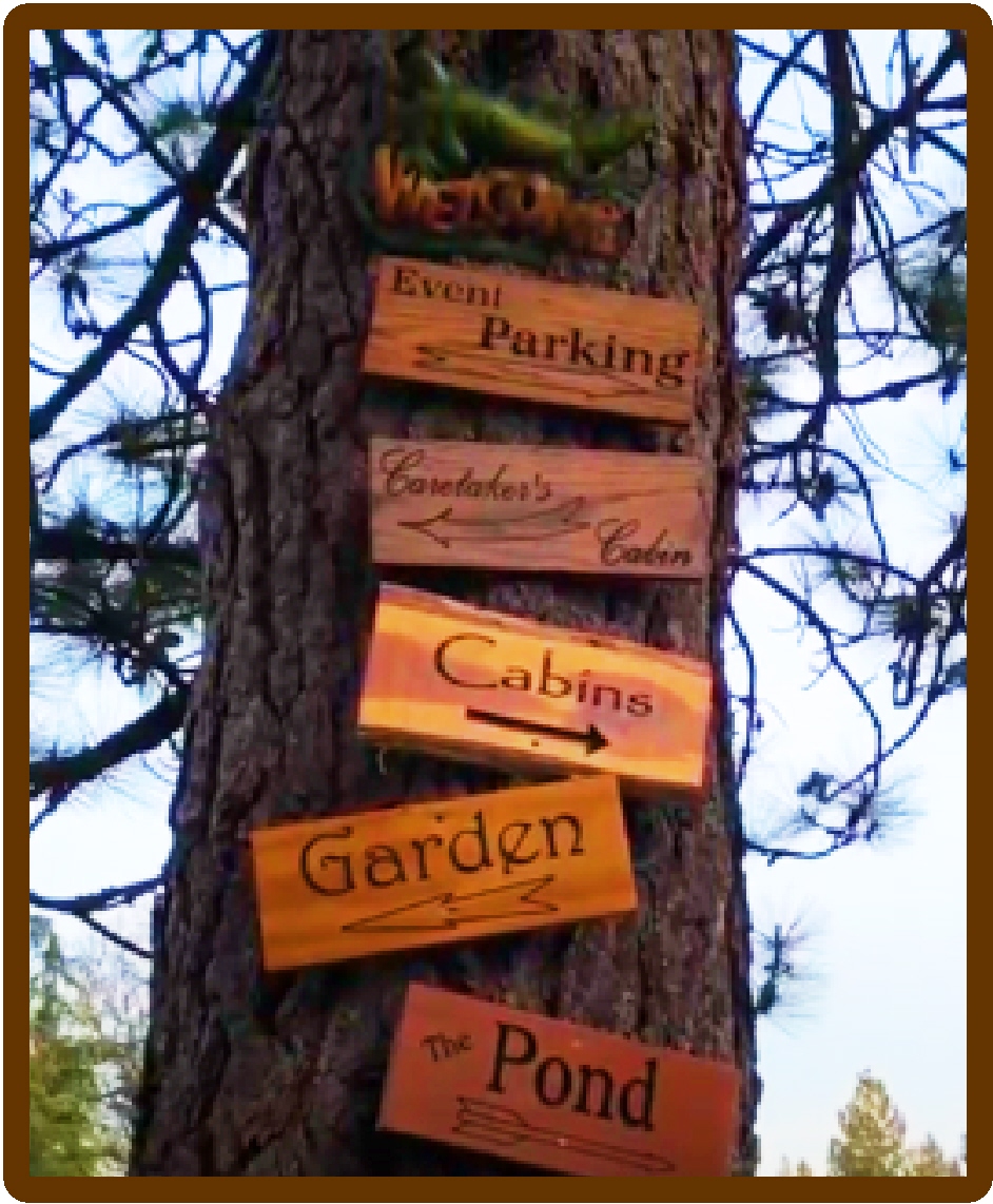 Wooden signs on tree directing to cabins, garden, pond, and parking.