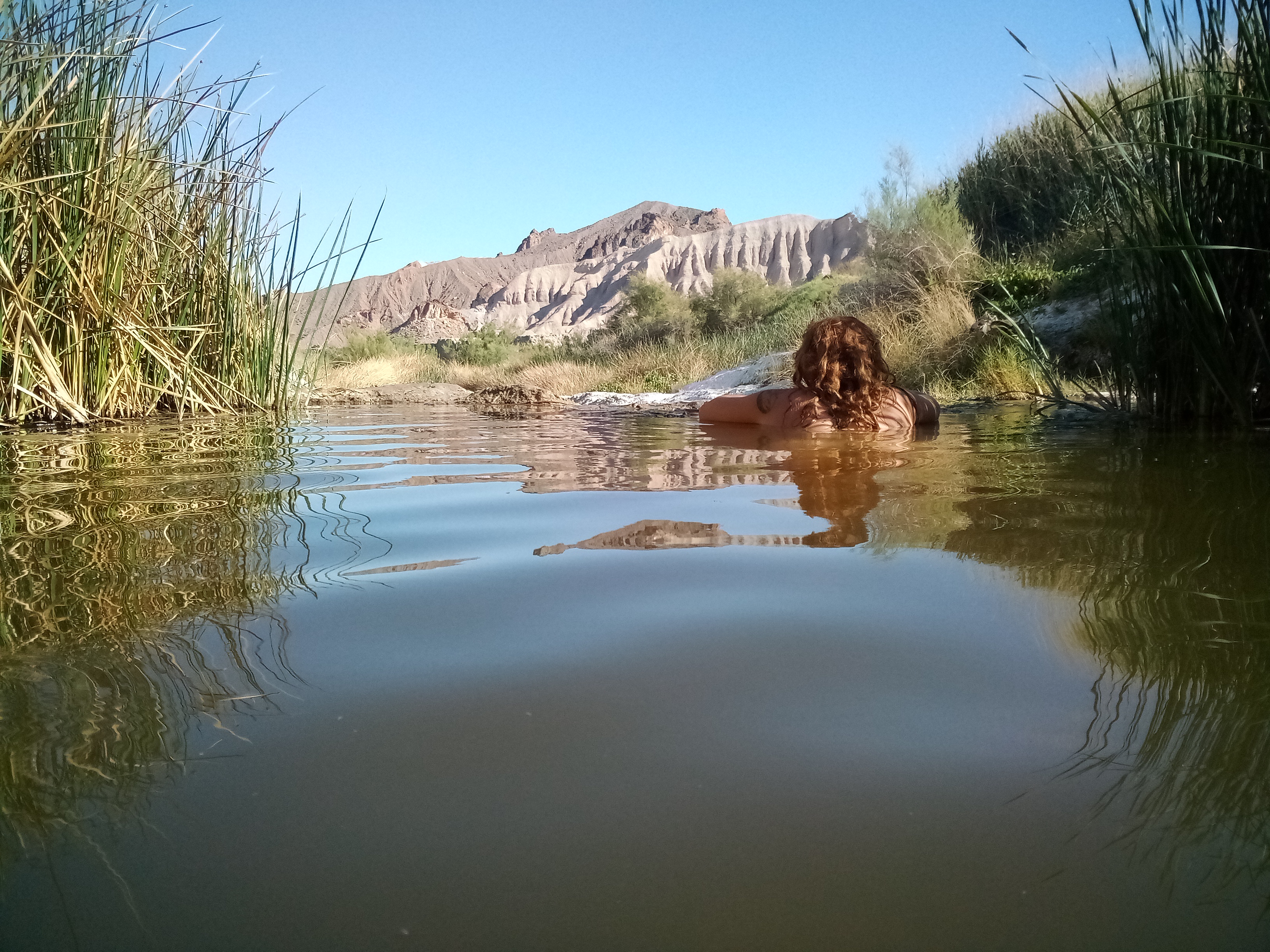 Person relaxing in river surrounded by nature and mountains.