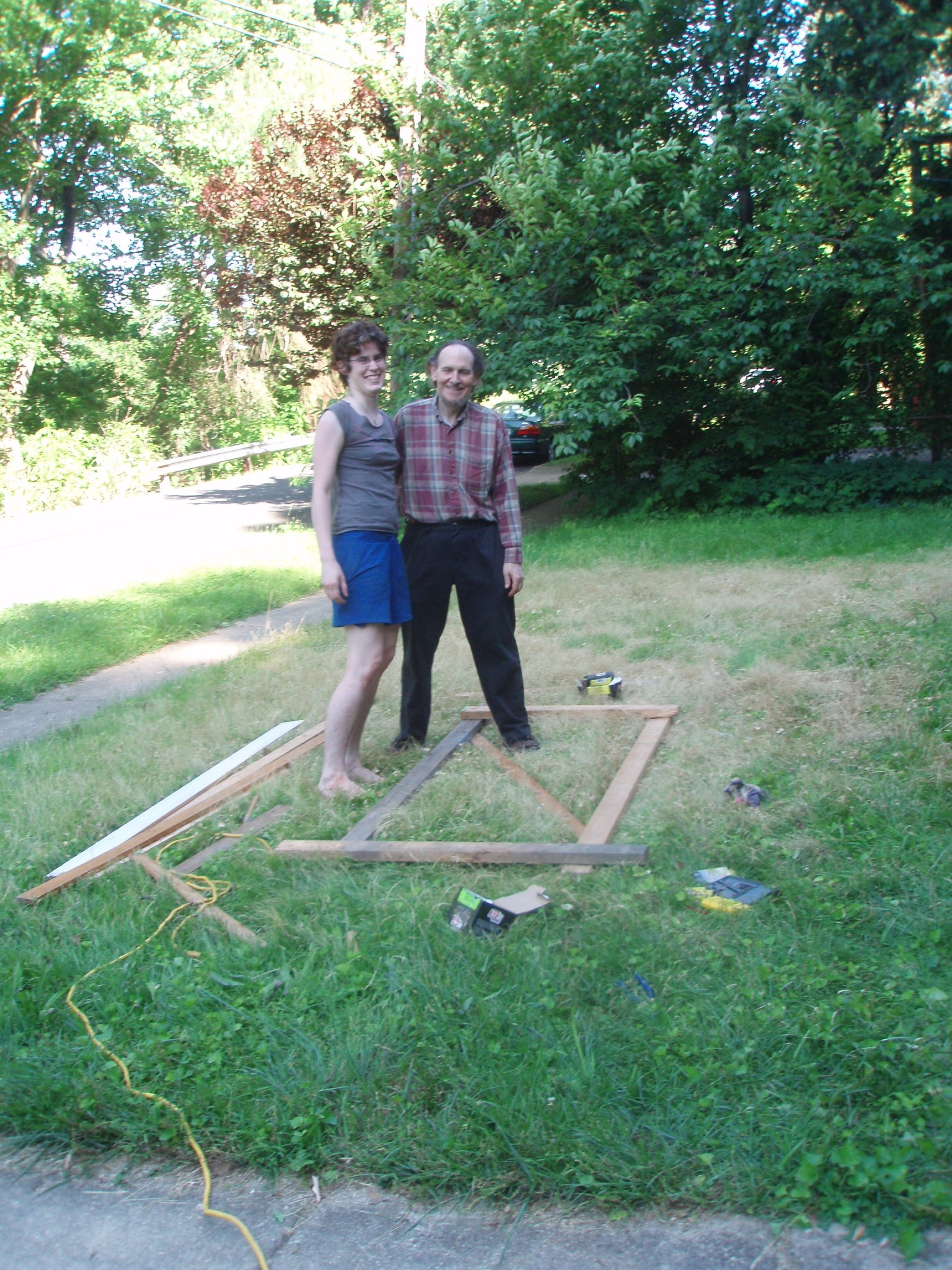 Two people building a garden frame outdoors in a green park.