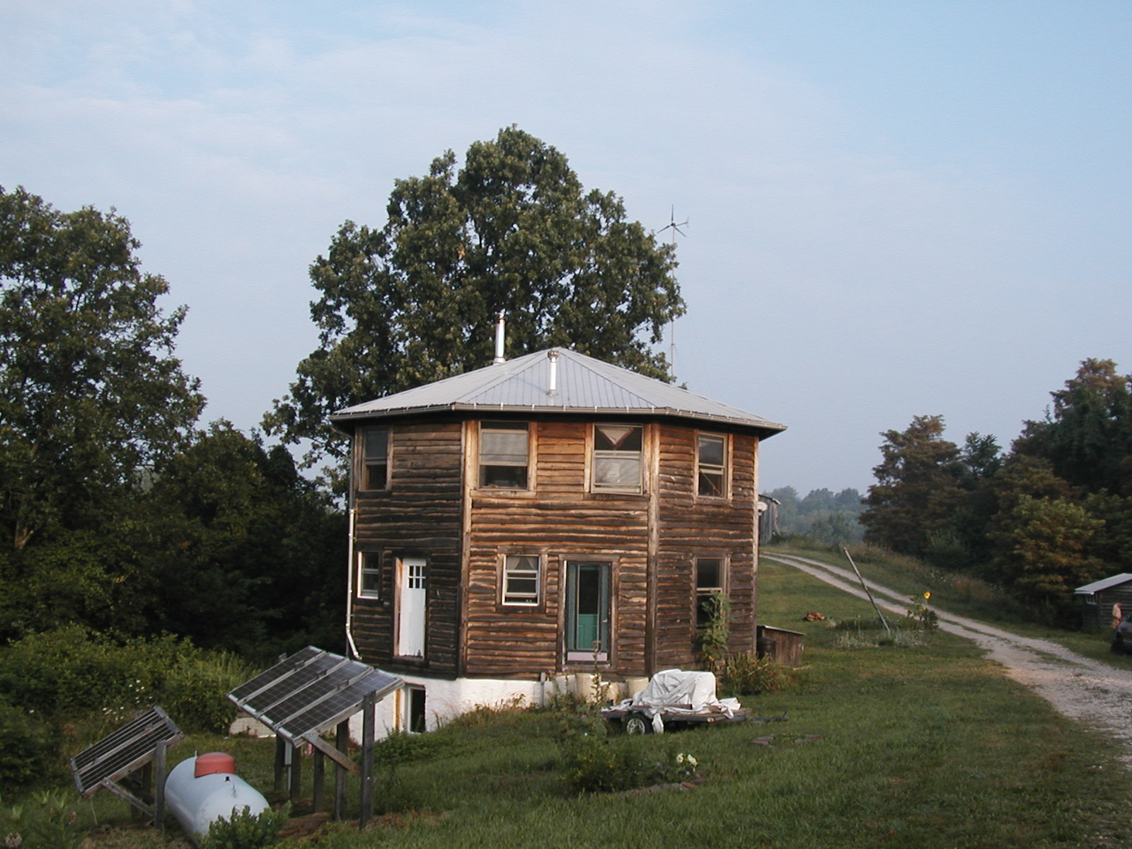 Round wooden community house with solar panels and surrounding greenery.