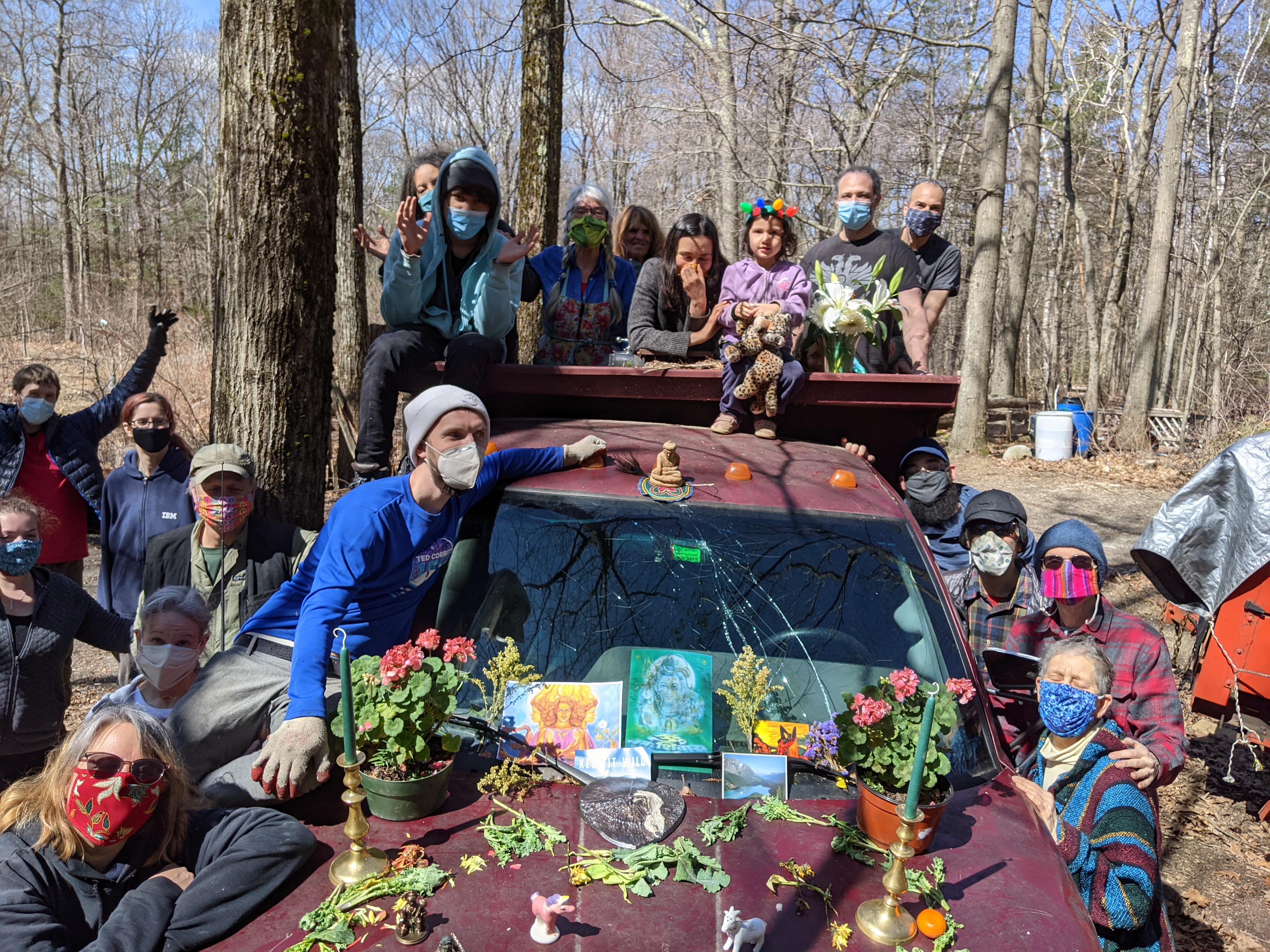 Group of people outdoors with decorated car and flowers in a forest setting.