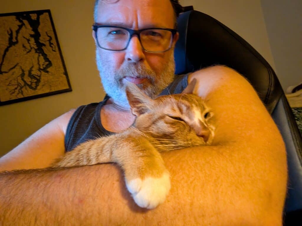 Person with glasses cuddling a cat in a cozy indoor setting.