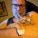 Person with glasses cuddling a cat in a cozy indoor setting.