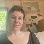 Woman sitting indoors with natural light and artwork in background.