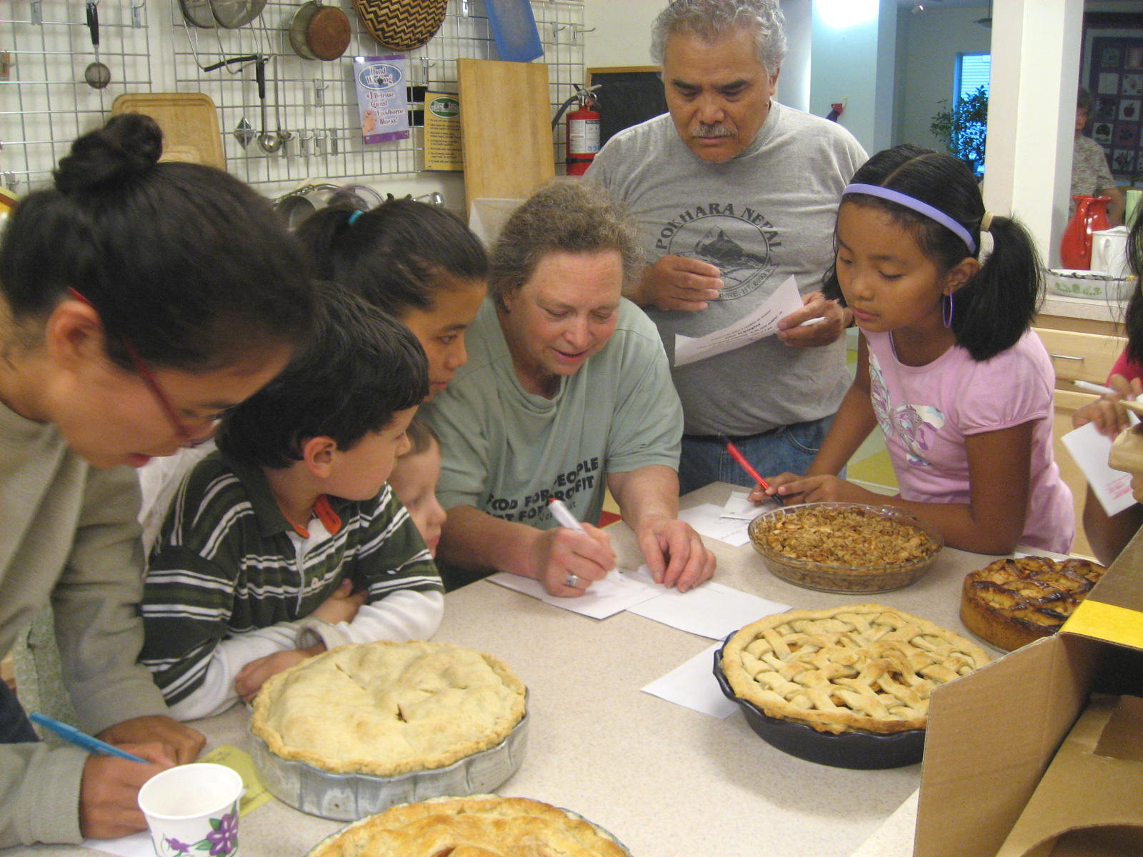 Group of children and adults baking and preparing pies together in a community kitchen.