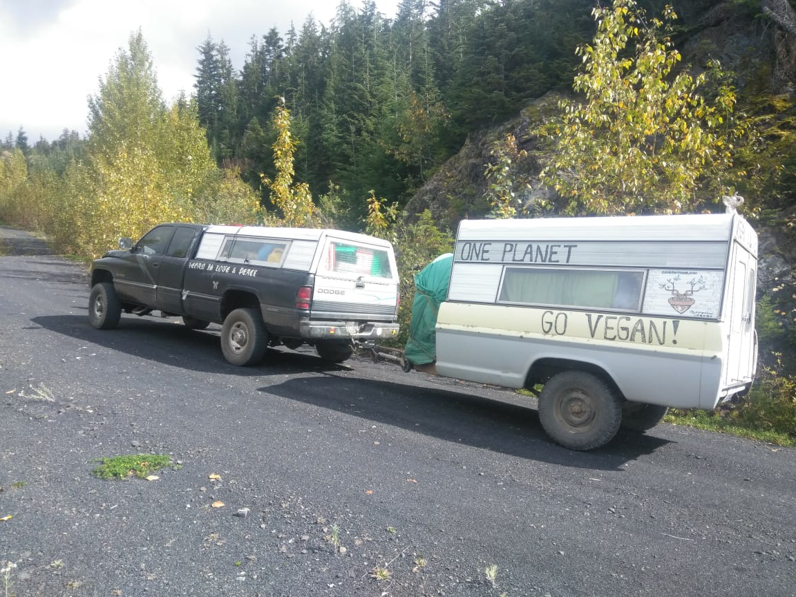 Camper trailer with vegan message hitched to a car in nature setting.