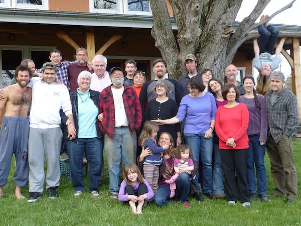 Group of diverse people gathered outdoors near a large tree at Canaan Village.