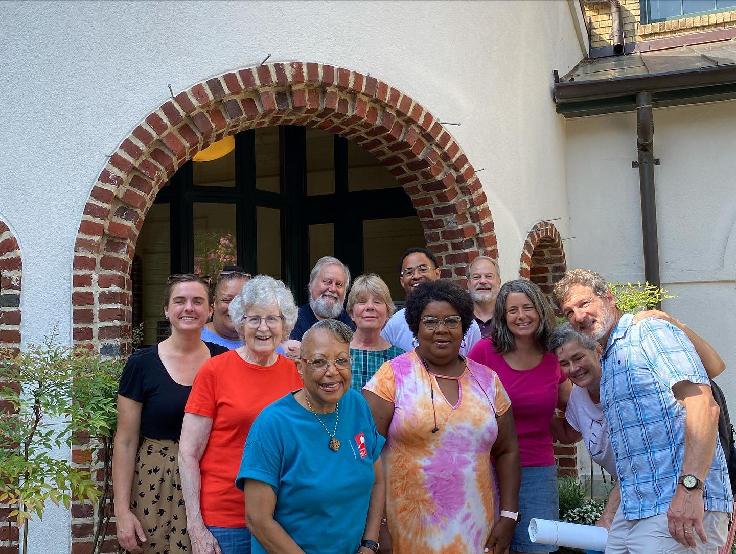 Diverse group of people smiling outside a building with brick archway.