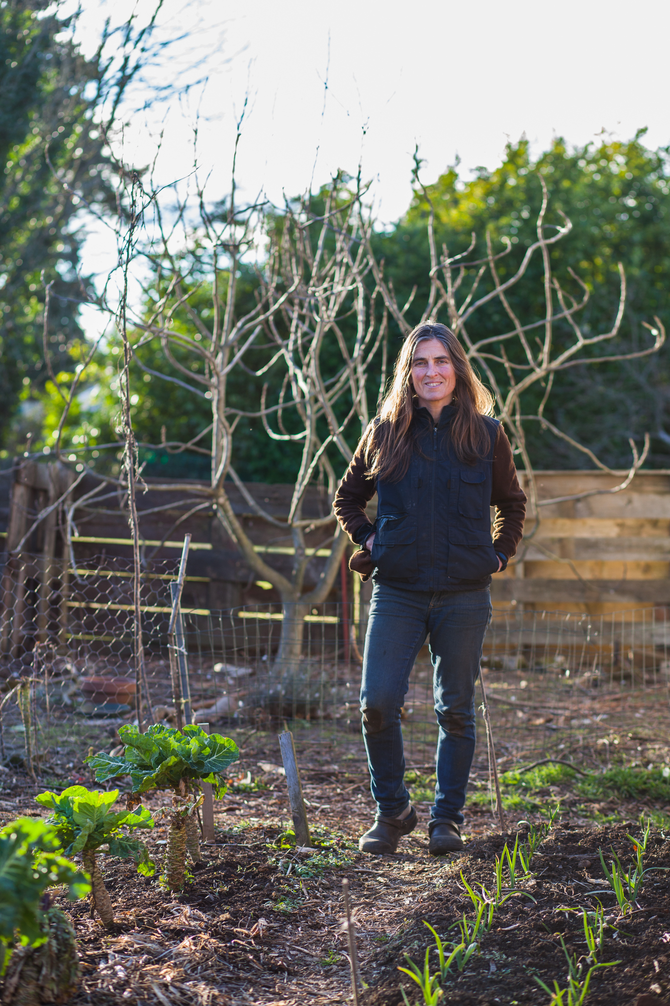 Woman standing in community garden with trees and plants.