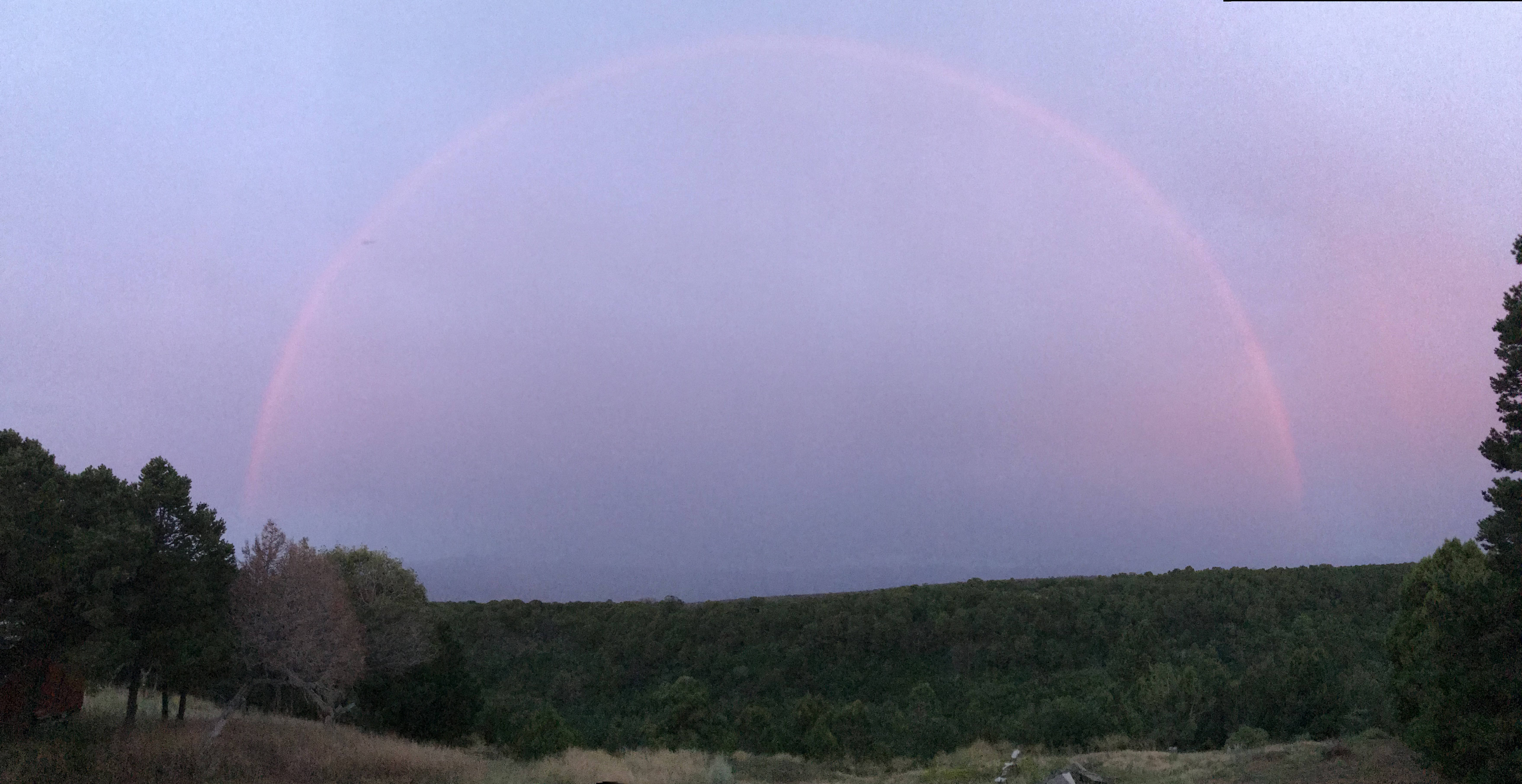 Rainbow arching over a green landscape in Colorado at sunset.