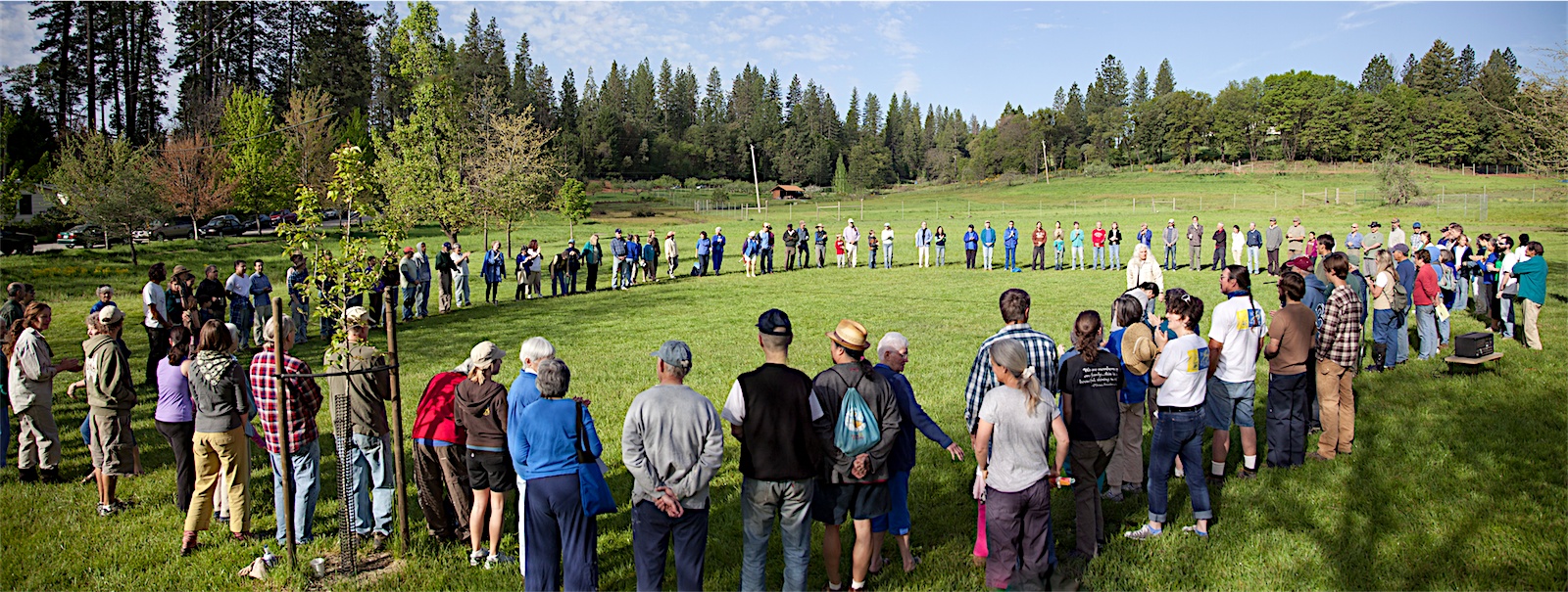 People forming a large circle on a grassy field at Ananda Village.