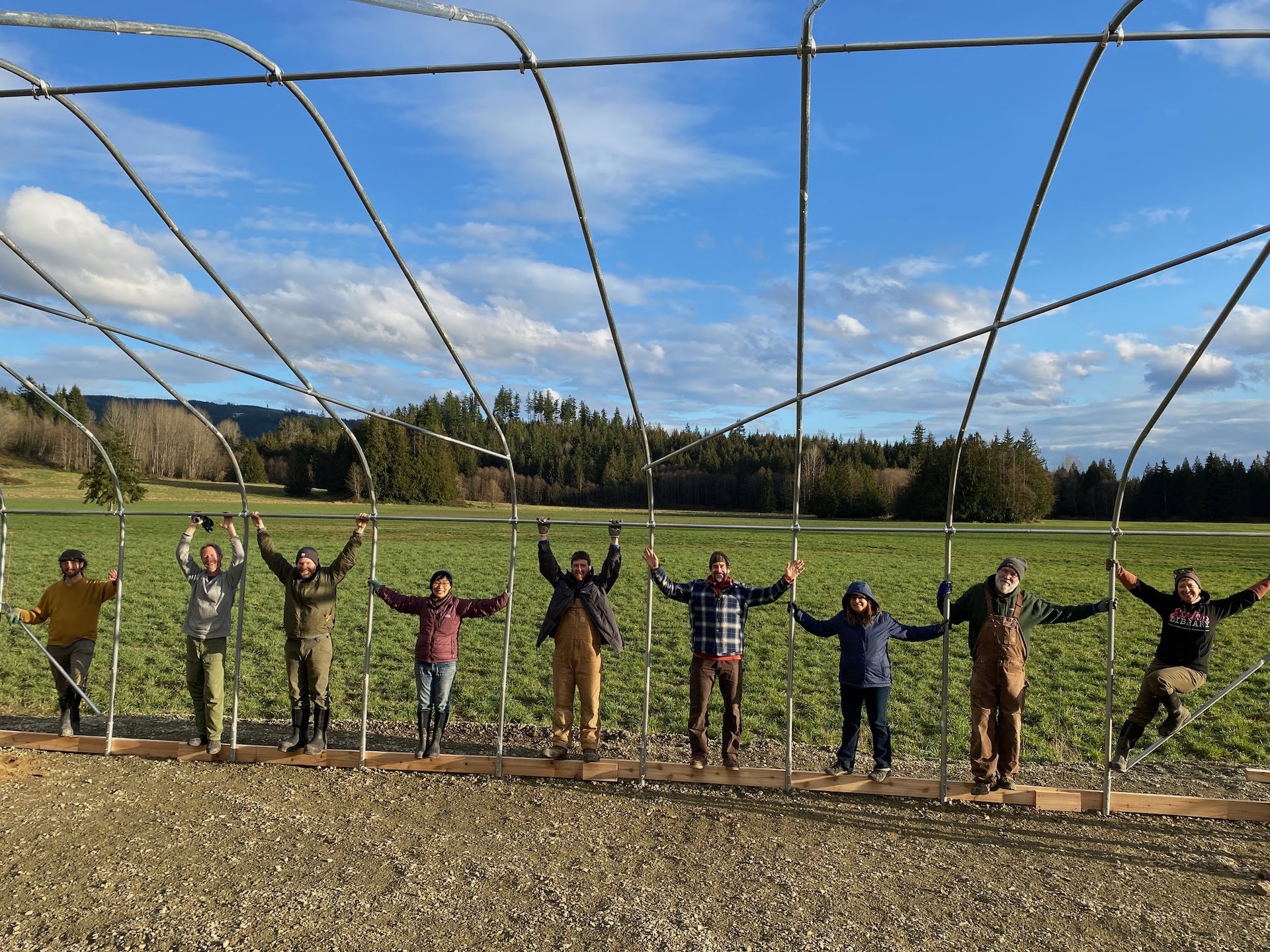 People working together to build a greenhouse structure in a rural setting.