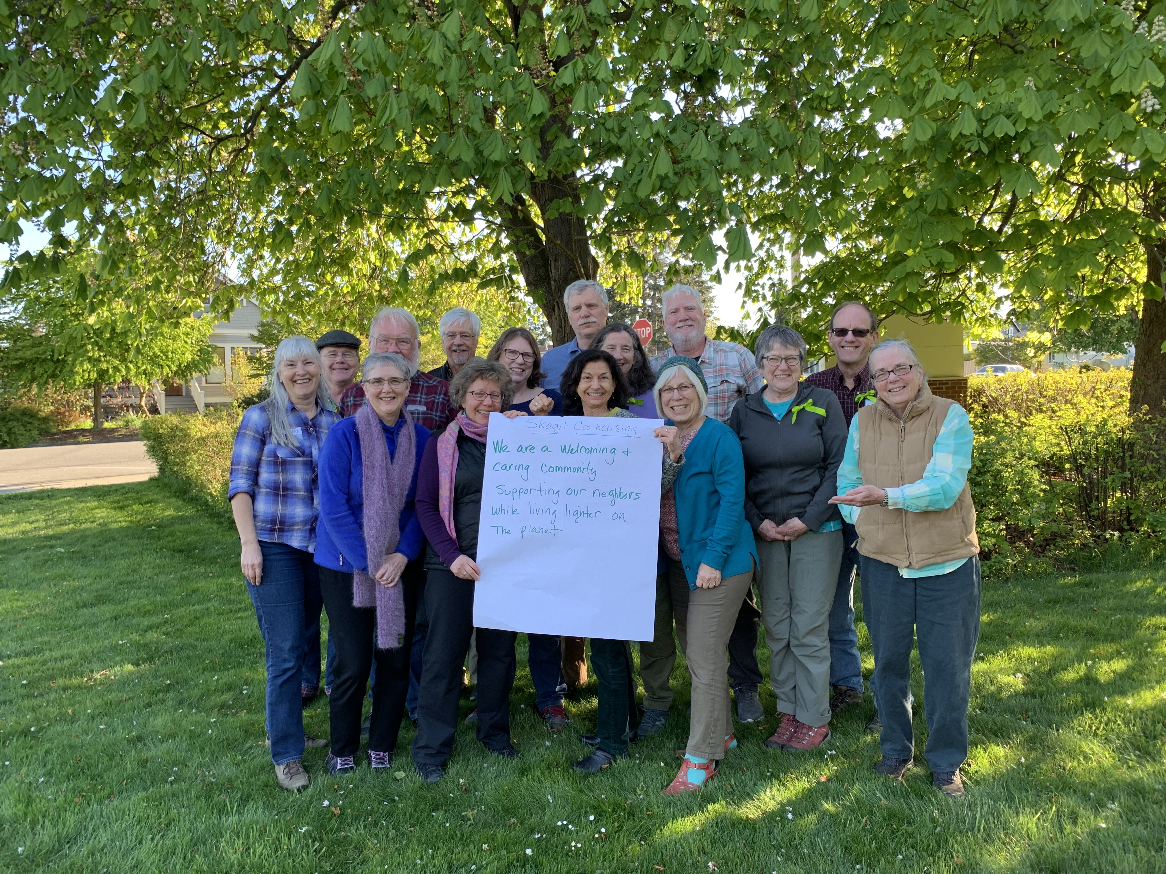 Group of diverse community members holding a sign outdoors under a large tree.