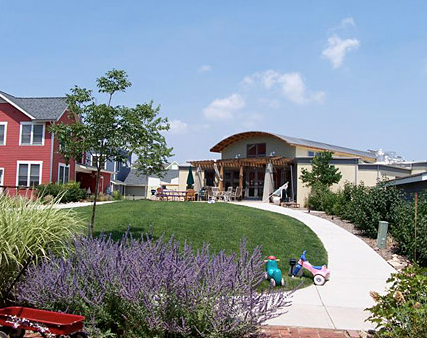Outdoor community space with a curved pathway, greenery, and a building in the background.