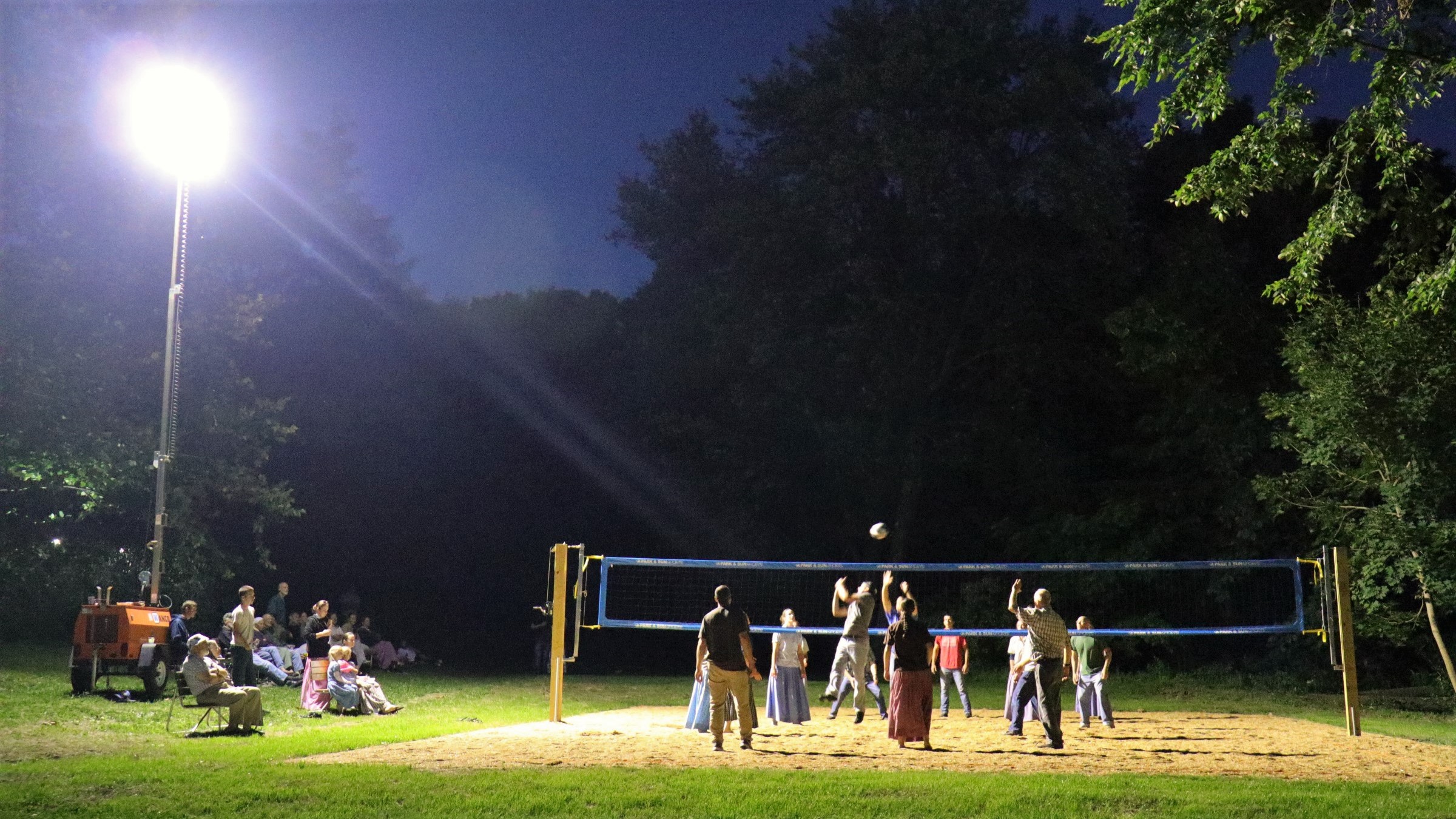 People playing volleyball on a lit outdoor court at night.