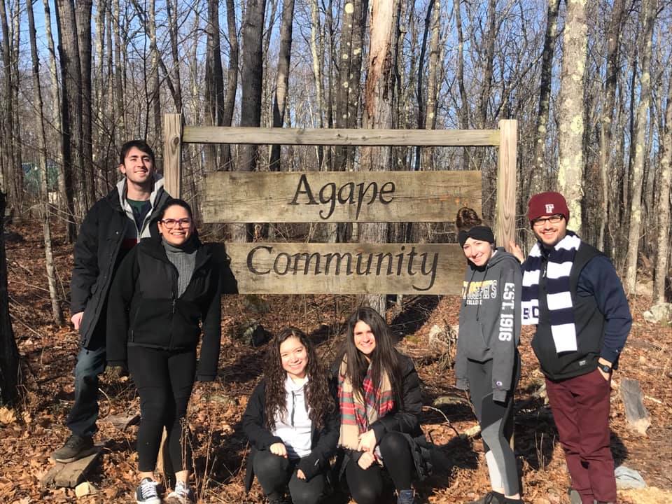 Group of diverse people at Agape Community sign in wooded area.