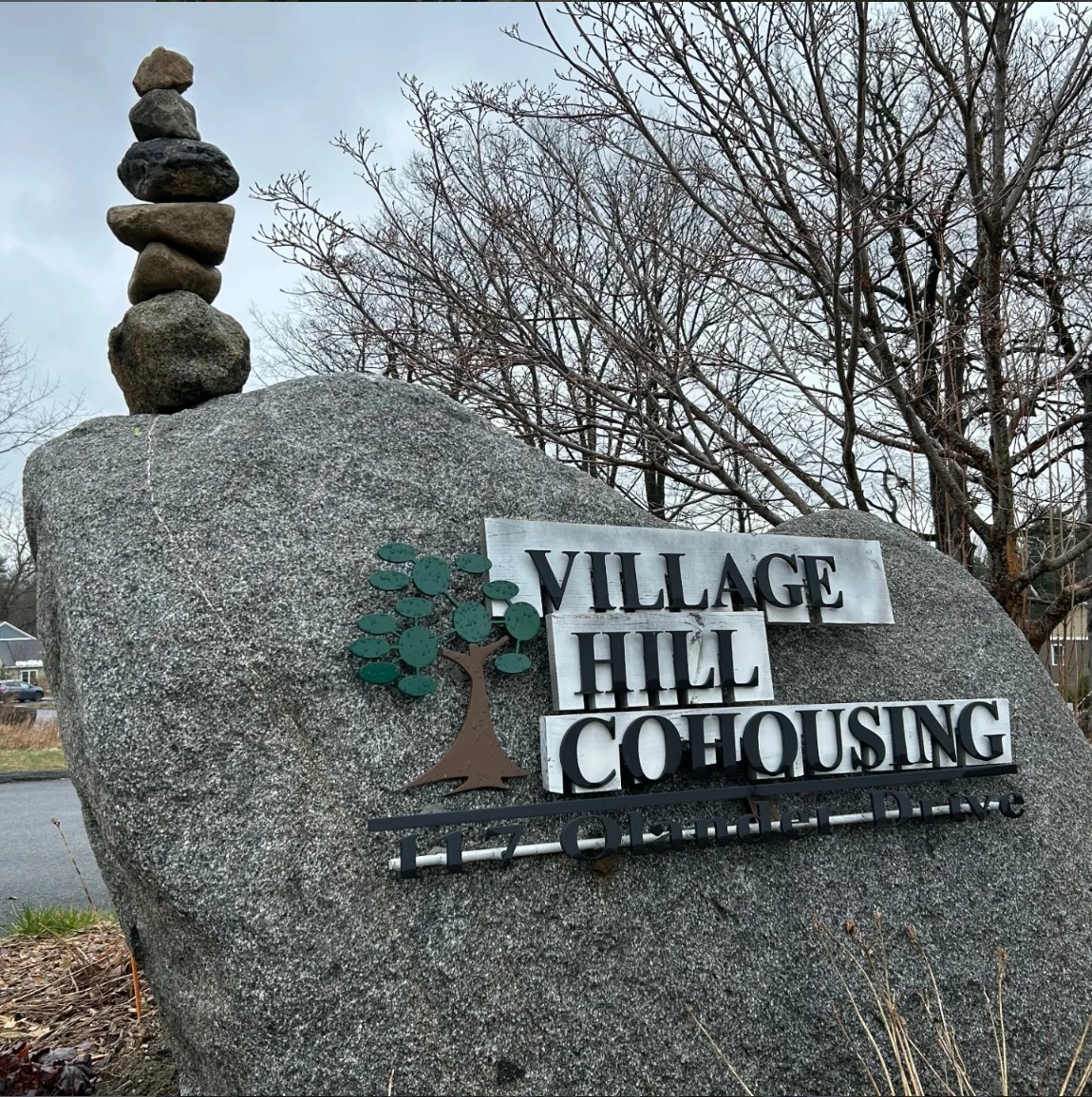 Village Hill Cohousing sign on a large rock with trees in background.