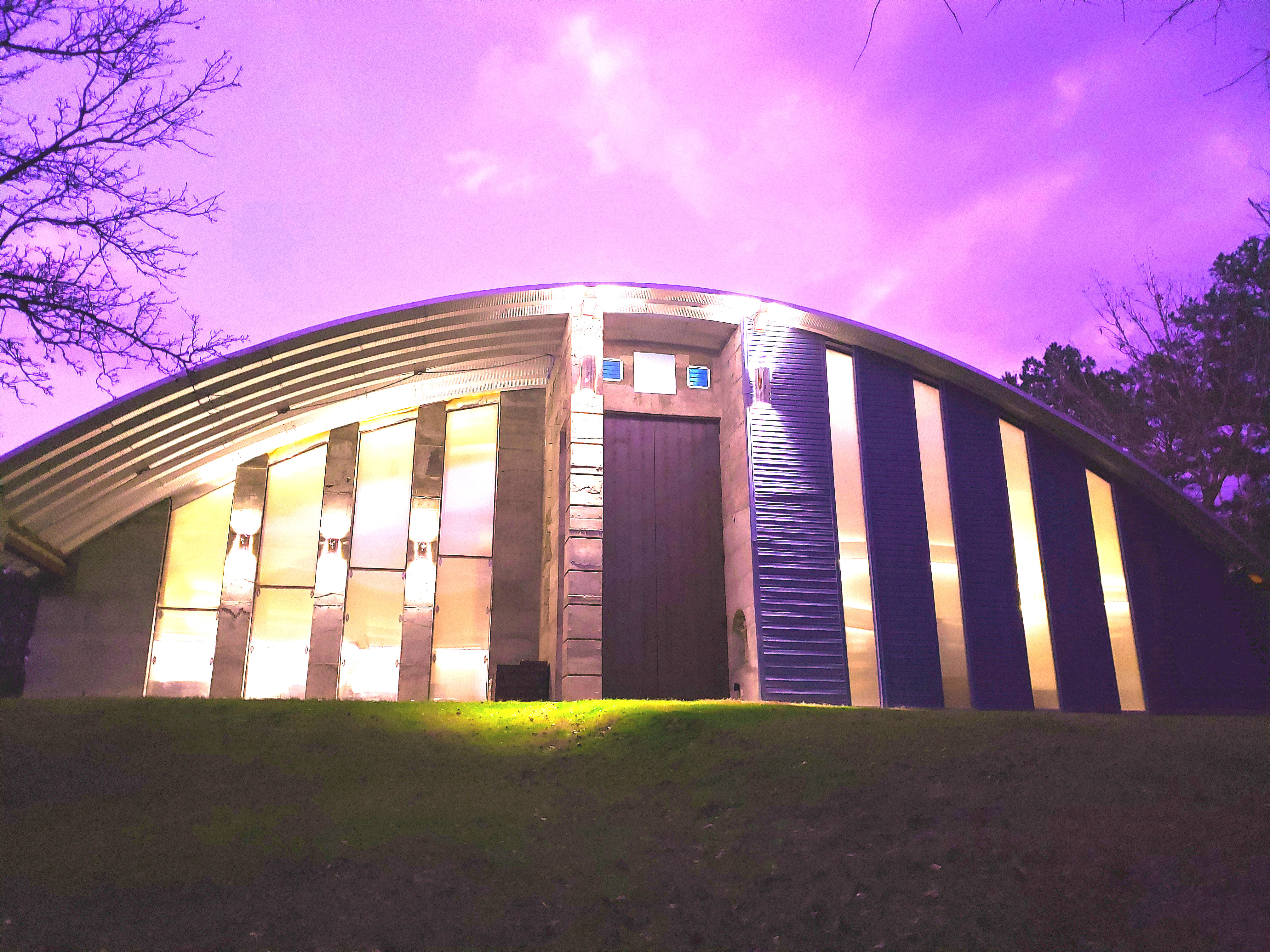 Modern community center with curved roof and vertical windows under purple sky.
