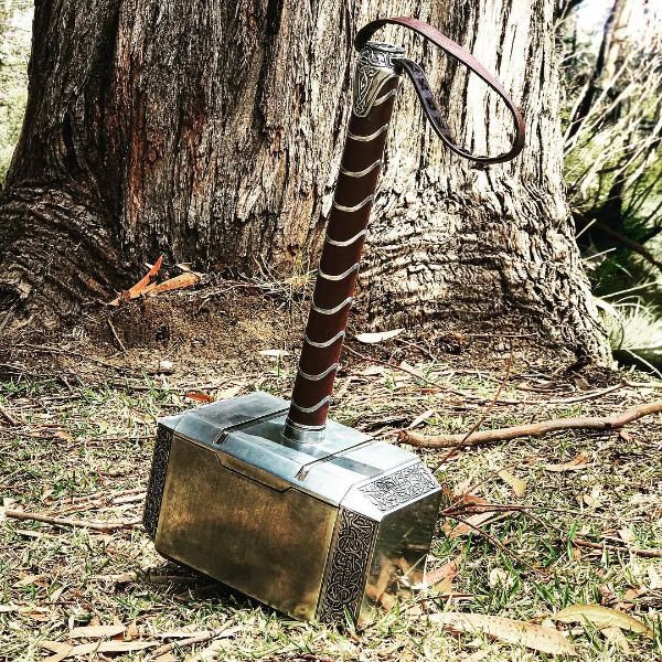 Hammer resembling Mjolnir with a leather-wrapped handle on forest ground.