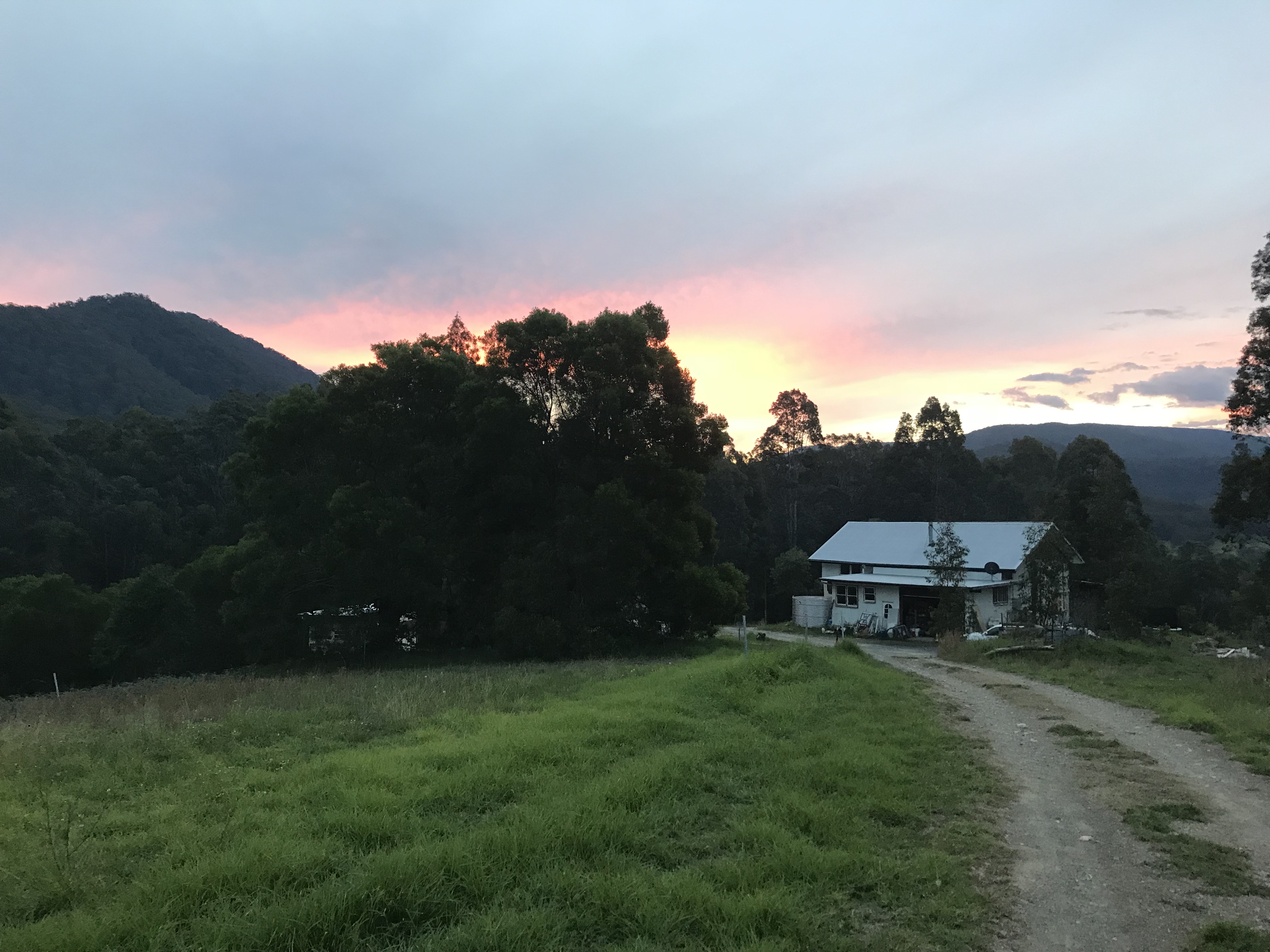 Beautiful rural landscape with a house, trees, and mountains at sunset.
