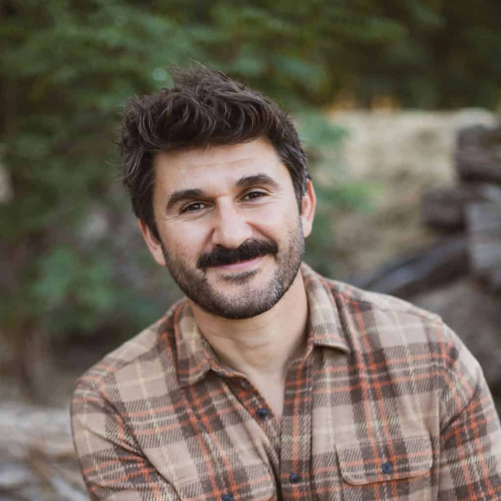 Smiling man outdoors with trees and rocks in the background.