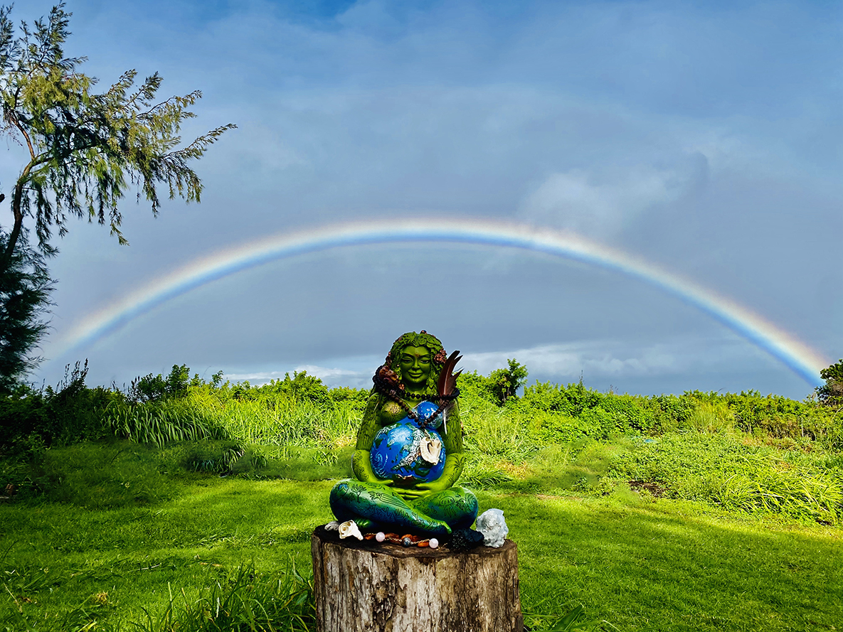 Colorful statue of a meditating figure with rainbow in background.
