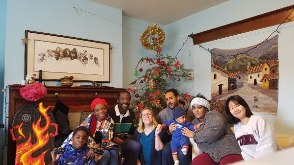 Group of diverse people celebrating around a Christmas tree in a cozy room.