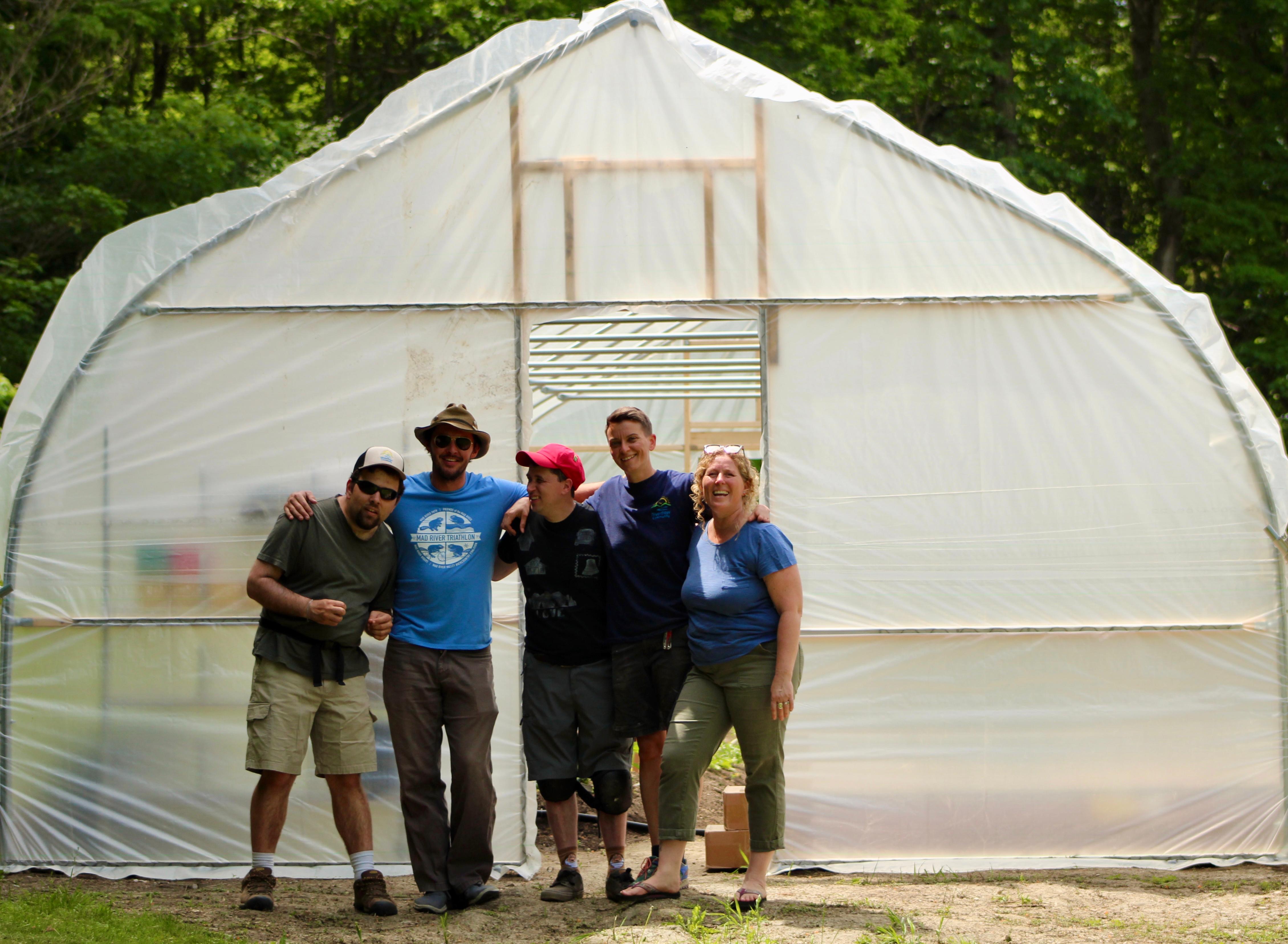 Group of people standing in front of a greenhouse at Riverflow Community.
