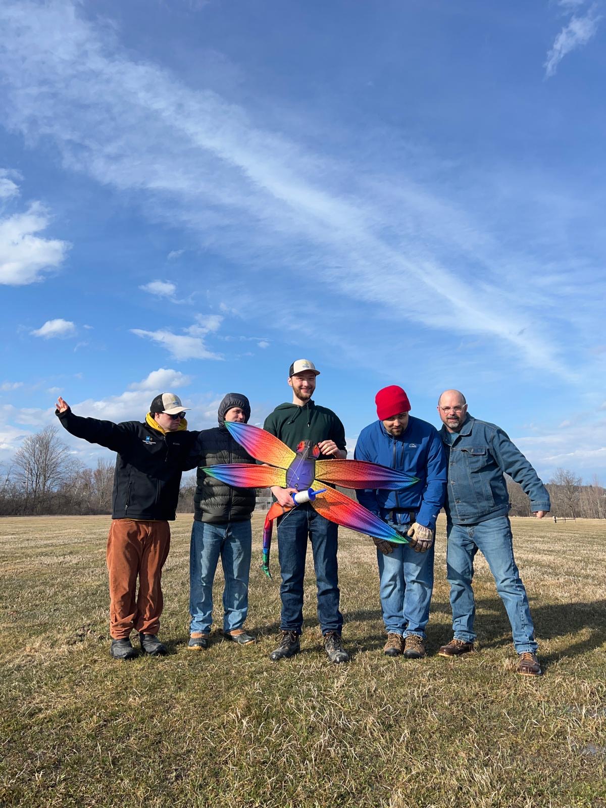 Group of people holding a vibrant kite outdoors in a grassy field.