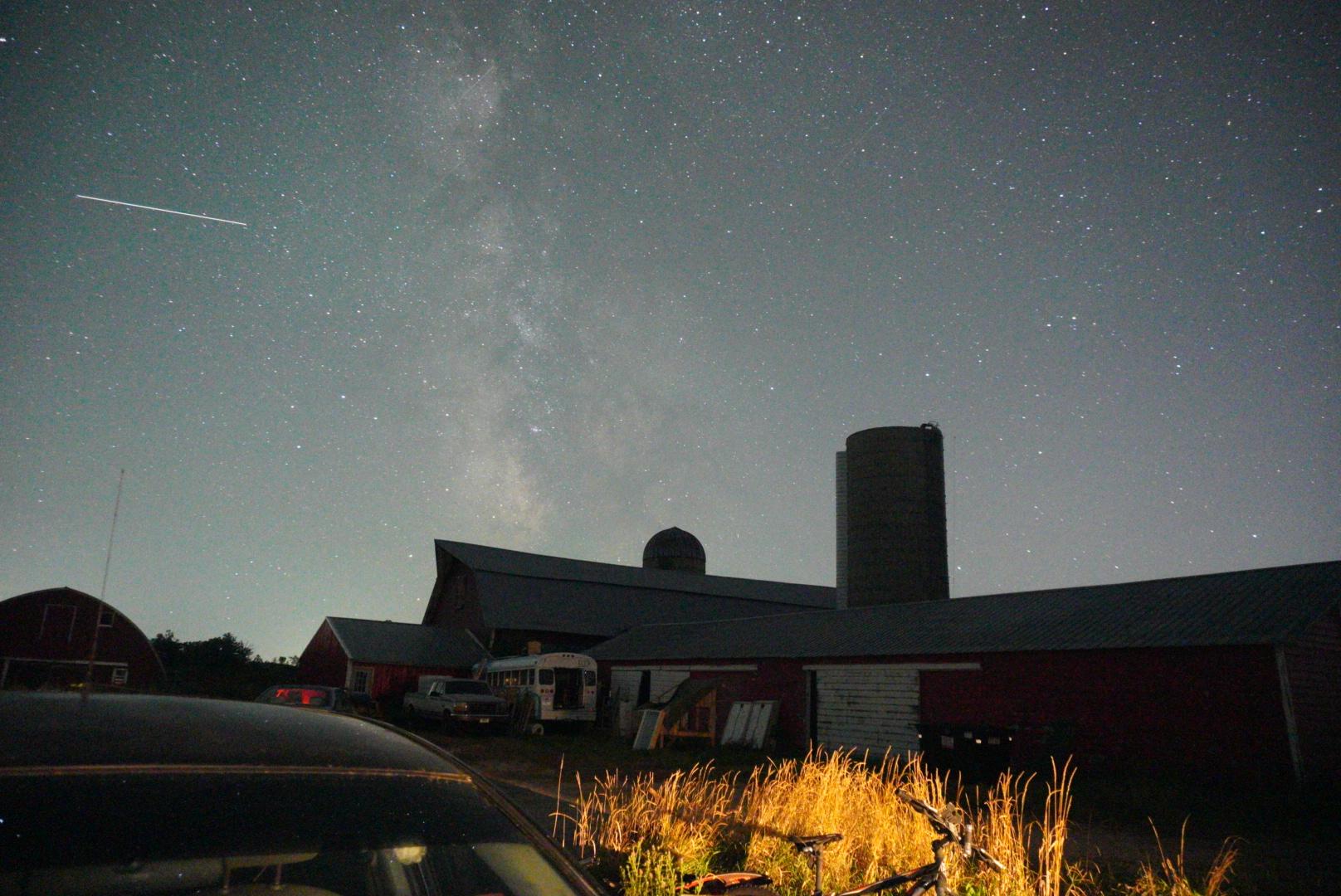Night sky filled with stars and the Milky Way over a farm with barns and silos.