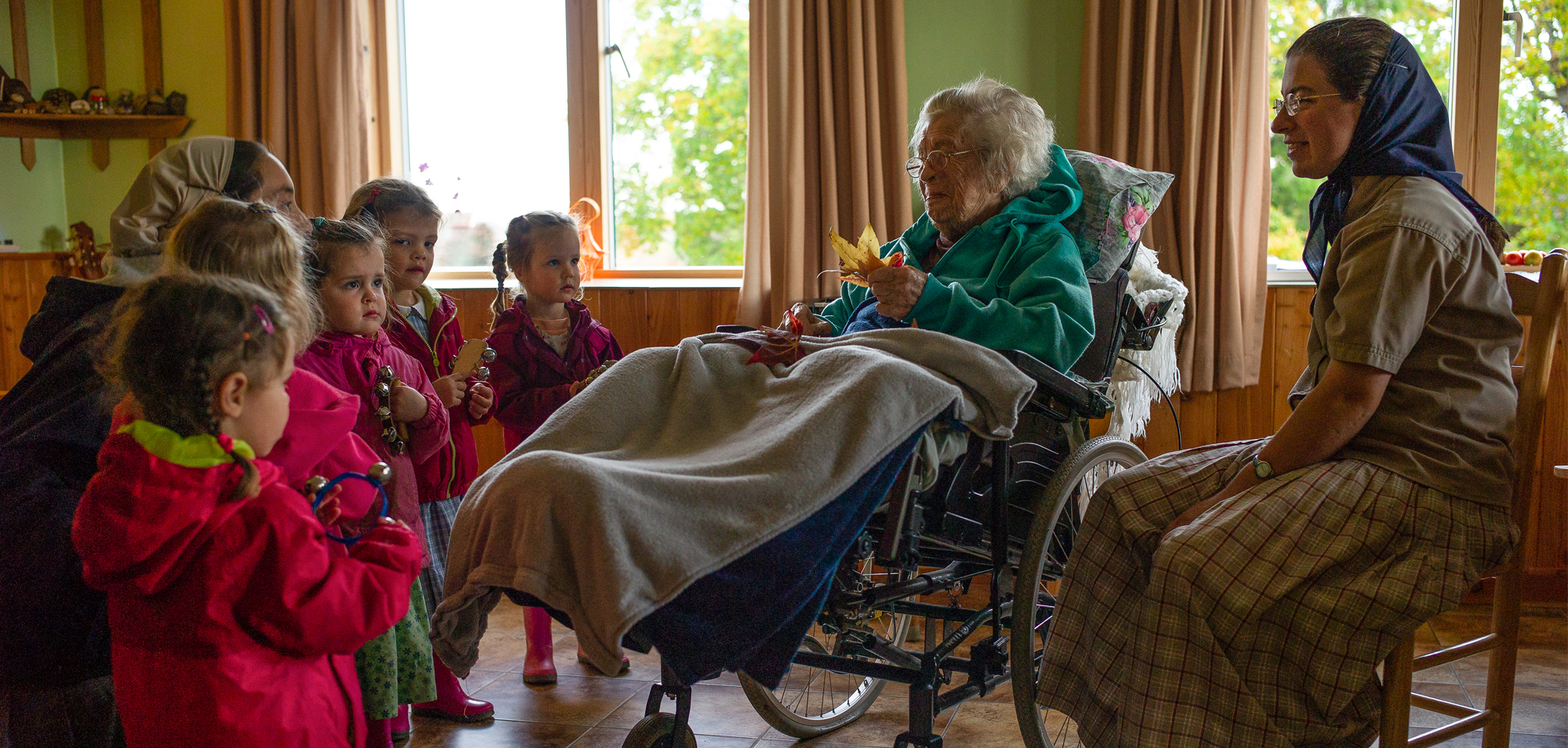Elderly woman in wheelchair with children visiting in a cozy room.