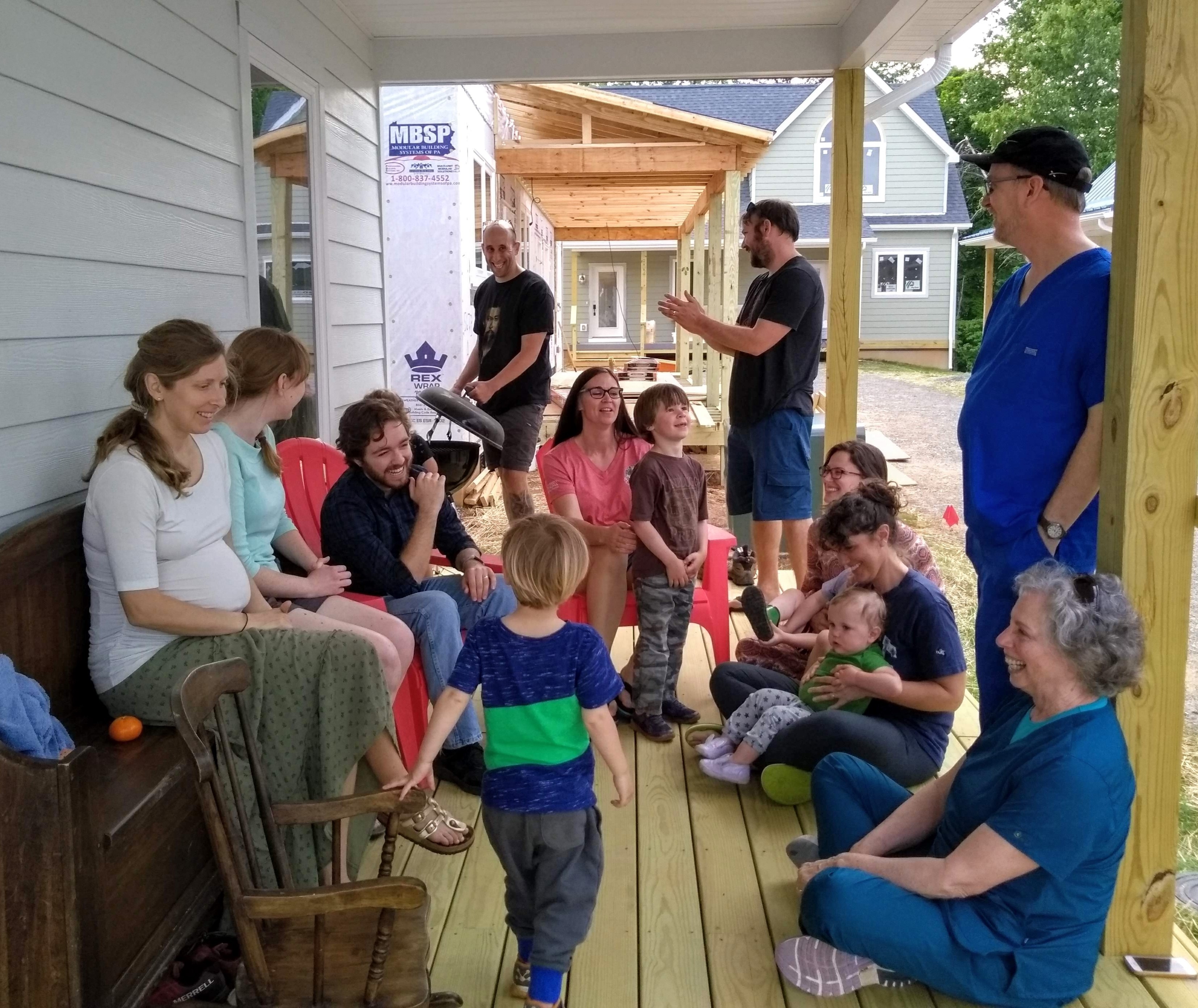 Group of people, including children, gathered on porch during community event at Emerson Commons.
