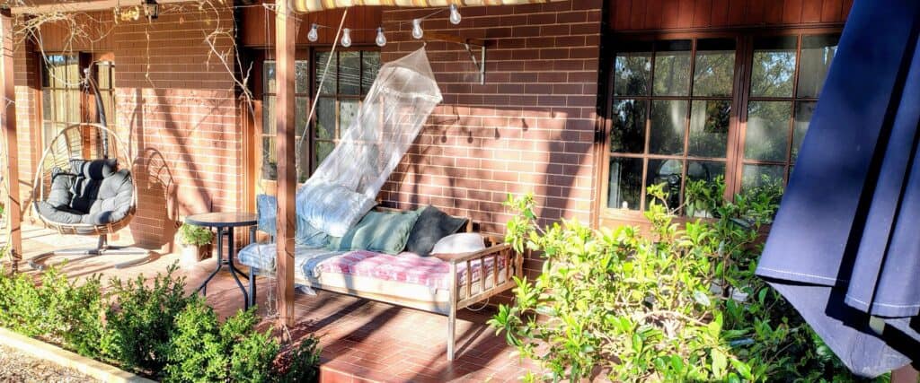 Cozy outdoor porch with a swing, cushioned bench, and lush plants.