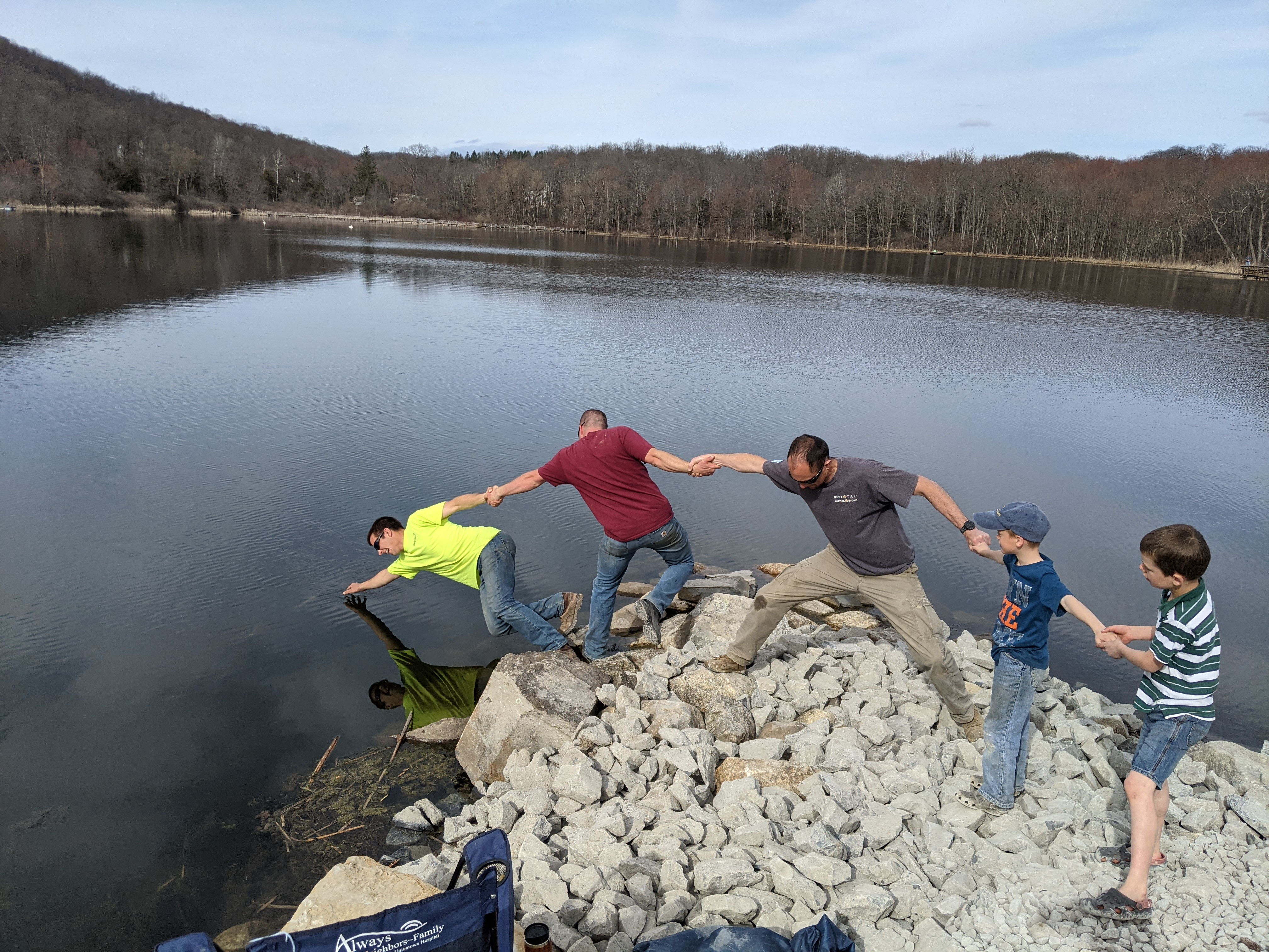 People holding hands across rocks by a lake at Bellvale Bruderhof Community.