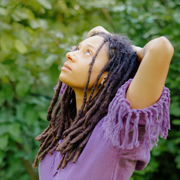 Woman with dreadlocks enjoying nature, looking up peacefully.