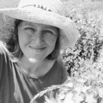 Woman smiling in sun hat in garden, enjoying outdoor nature scene.
