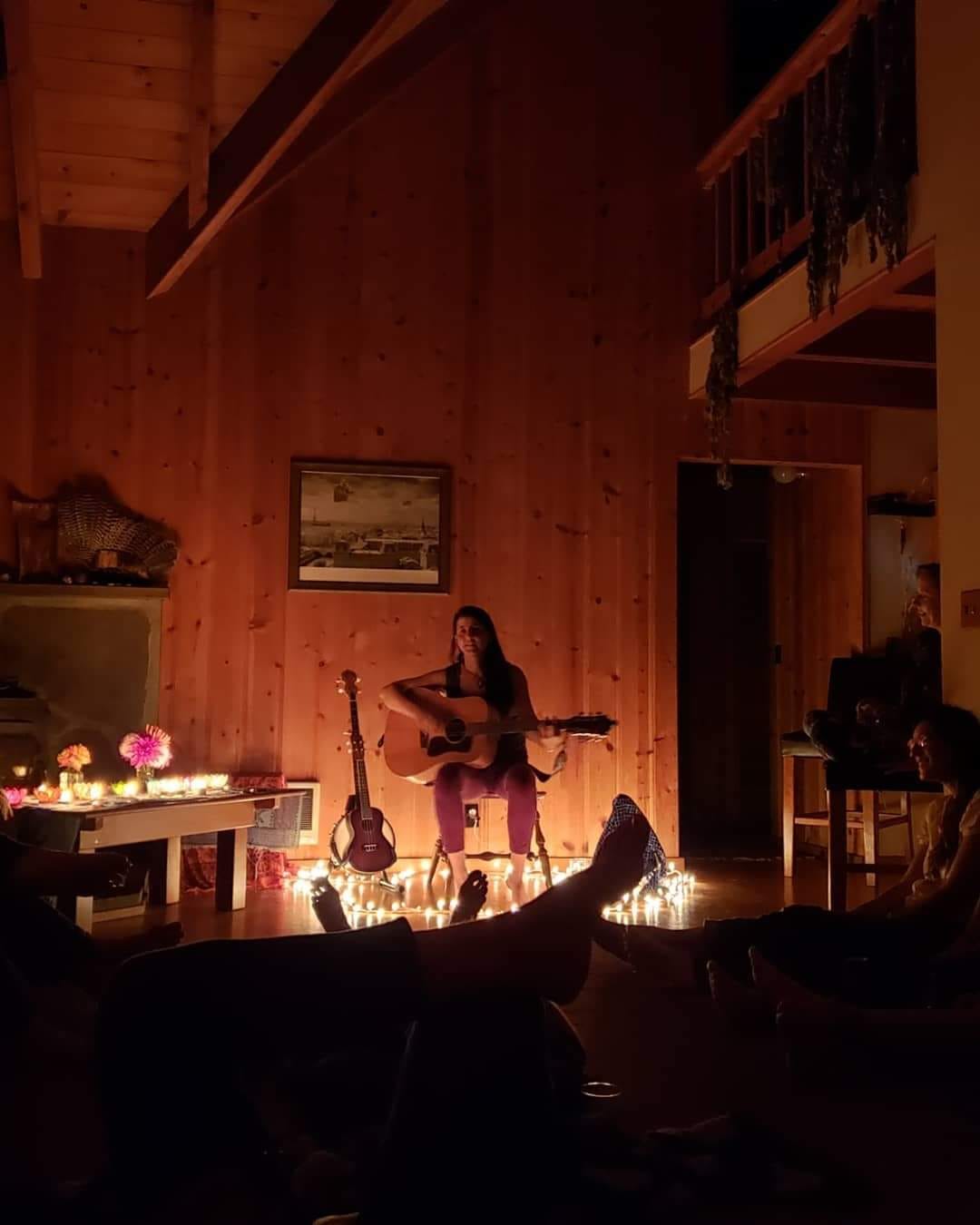 Person playing guitar at community event in cozy wooden space.