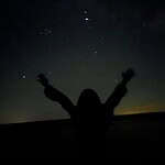 Silhouette of person with raised arms under starry night sky.